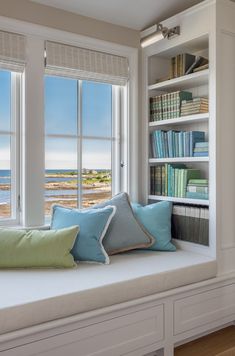 a window seat with bookshelves and pillows on it in front of two windows