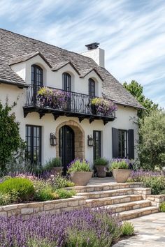 a white house with black shutters and flowers in the front yard on a sunny day