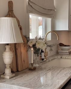 a white kitchen with marble counter tops and gold faucet light on the sink