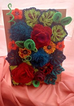 a wooden box with crocheted flowers in it on a pink cloth covered surface