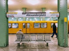 two people sitting on benches in front of a yellow train at the subway station while another person walks by