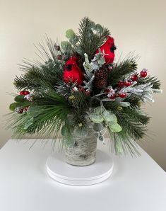 a vase filled with red flowers and greenery on top of a white table next to a wall