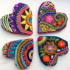 four pieces of colorful embroidered heart shaped appliques on a white surface, each with different designs and colors