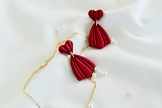 two red necklaces with pearls on a white cloth covered surface, one is attached to a gold chain and the other has been made out of paper