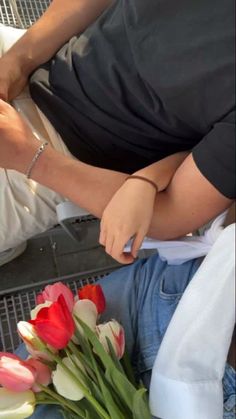 two people sitting next to each other with flowers in front of them on the ground