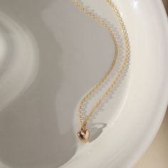 14k Everthine Necklace laid on a white plate sitting in the sunshine, This necklace features the simple chain along with the puff heart. Handmade in Eau Claire, Wisconsin.