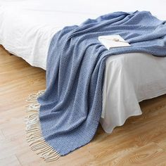 a bed with a blue blanket on top of it next to a white pillow and wooden floor