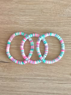 three bracelets are sitting on top of a wooden table, one is pink and the other is blue