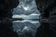 the sky is reflected in the still water at the edge of the cave, with dark clouds above