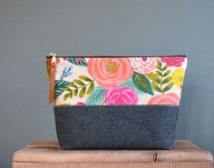 the zippered pouch is sitting on top of a wooden block with flowers and leaves