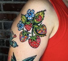 a woman's arm with flowers and strawberries on it, next to a brick wall