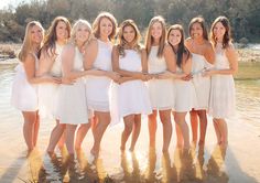 a group of beautiful women standing next to each other in front of a body of water