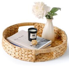 a wicker basket with a candle, vase and book on it next to a white flower