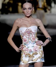 a model walks down the runway in a strapless white dress with floral designs on it