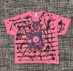 a pink t - shirt with black and red graffiti on the front, sitting on a gray surface