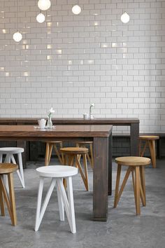 a table with four stools in front of white brick wall and lights above it