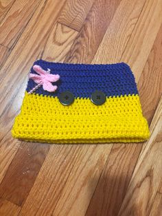 a crocheted yellow and blue hat with two black buttons on the top, sitting on a wooden floor