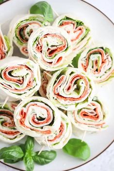 a plate filled with rolled up sandwiches on top of green leaves