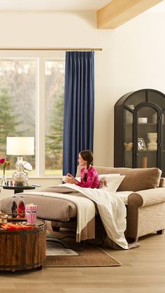 a woman sitting on top of a couch in a living room next to a window