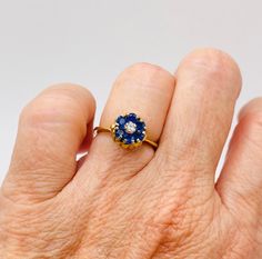 Give yourself a treat with this dainty little tulip ring in 18k yellow gold that's a timeless classic. Flowers are beautiful so why not put one on your finger? This ring weighs 3.4g and is a size 4.5. Studded with beautiful sapphires and a diamond in the middle, sapphires weighing 0.50 carats and the diamond weighing 0.06 carats, this ring is exactly what you need for your jewelry desires. Classic 14k Gold Flower Ring With Gemstone, Yellow Gold Solitaire Diamond Flower Ring, Elegant Yellow Gold Flower Ring With Birthstone, Classic Yellow Gold Sapphire Birthstone Ring, Classic Yellow Gold Sapphire Cluster Ring, Classic Sapphire Cluster Ring In Yellow Gold, Classic Yellow Gold Flower Ring With Prong Setting, Brilliant Cut Sapphire Birthstone Ring In Yellow Gold, Yellow Gold Sapphire Birthstone Ring With Brilliant Cut