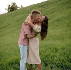 a man and woman are kissing in the middle of a grassy field on a hill