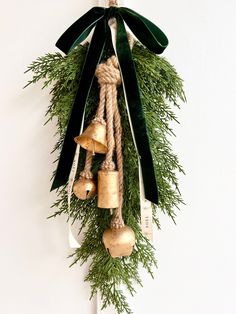 an evergreen wreath with bells hanging from it's sides and tied to the wall