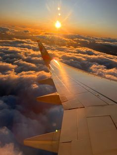 the wing of an airplane as it flies above the clouds at sunset or dawn with the sun peeking through the clouds