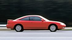 a red sports car is driving down the road with trees in the backround