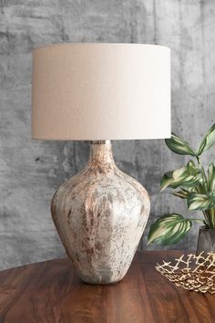 a table with a lamp on it next to a potted plant and a basket