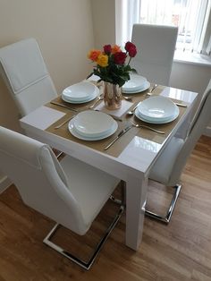 a dining table with white chairs and plates on it