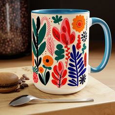 a coffee mug sitting on top of a wooden table next to a spoon and cookie