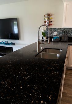 a black counter top in a kitchen next to a tv mounted on the side of a wall