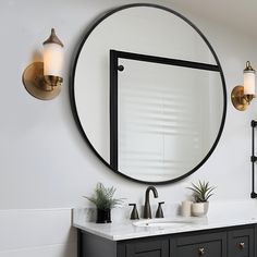 a bathroom vanity with a round mirror above it and two plants on the counter top