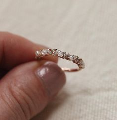 a hand holding a diamond ring in it's left hand on a white cloth