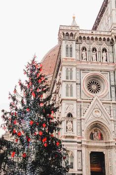 a large christmas tree in front of a church with red ornaments on it's branches