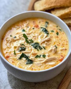 a white bowl filled with chicken and cheese soup next to bread on a cutting board