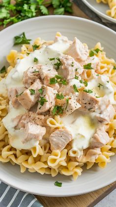 a white plate topped with pasta covered in chicken and sauce on top of it next to parsley