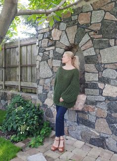 a woman standing in front of a stone wall with her head turned to the side