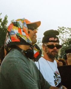 two men in hats and sunglasses are talking to each other at an outdoor event while others look on