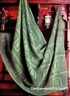 a green crocheted blanket sitting on top of a wooden table next to a potted plant