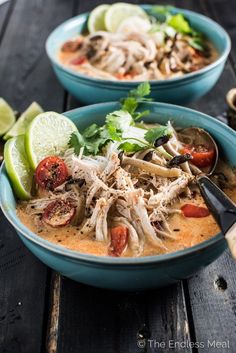 two bowls filled with soup on top of a wooden table next to sliced limes