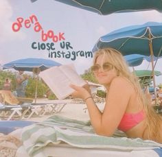 a woman laying on top of a beach next to umbrellas and reading a book