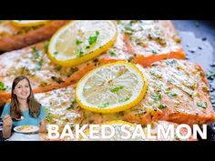 a woman sitting in front of baked salmon with lemons and parsley on the side