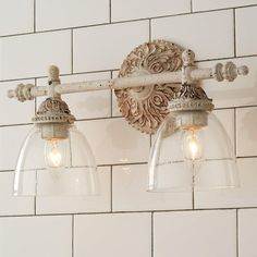 two lights are attached to the wall in front of a white brick wall and tile