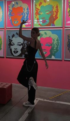 a woman is dancing in front of colorful paintings on the wall and holding her hand up