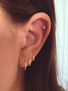 a close up of a woman's ear with three small gold hoops on it