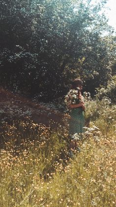 a woman standing in tall grass holding flowers