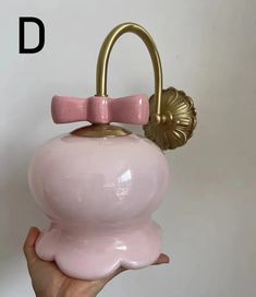 a hand holding a pink piggy bank with a gold handle and a bow on it