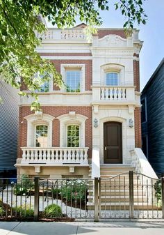 a large brick house with white railings on the front and second story, surrounded by trees