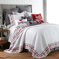 a white bed with red and gray pillows on it's sides, along with christmas decorations